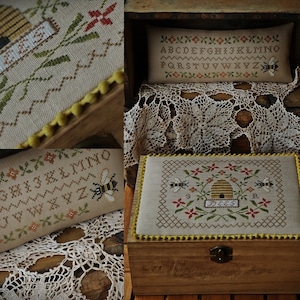 Może przedstawiać: Drewniana skrzynia z pokrywą na zawiasach, ozdobiona haftem krzyżykowym przedstawiającym ul i pszczoły. Pokrywa jest ozdobiona żółtą obwódką z koralików. Skrzynia stoi na drewnianej powierzchni.