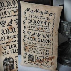 以下が含まれることがあります： 黒い刺繍が施された白い枕。刺繍にはアルファベット、日付「Oct 31, 1779」、そして「Ann Black」と「When this you see think of me」というテキストが含まれています。
