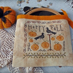 May include: A beige fabric bag with a brown embroidery hoop and orange trim. The embroidery features black birds, pumpkins, and the text "Happy Fall".