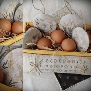 Puede incluir: Una caja de madera llena de huevos marrones, círculos de tela blanca y marrón con diseños bordados y una almohada de tela blanca con el alfabeto bordado.