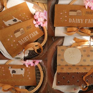 May include: Hand-stitched fabric pouches with a dairy farm theme. The pouches are a warm brown color and feature embroidered images of cows, barns, and the text "DAIRY FARM 1882". Each pouch is tied with a gold ribbon.
