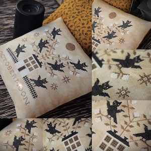 Puede incluir: Cojín beige bordado a punto de cruz con temática de Halloween. El diseño presenta gatos negros, una casa y el texto "OCTOBER MOON". El cojín tiene un patrón decorativo de ramas, flores y estrellas.