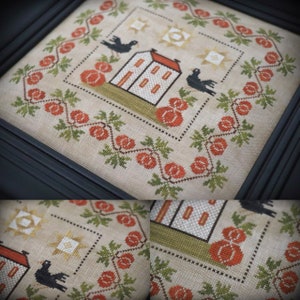 May include: Cross stitch pattern featuring a white house with a red roof, two black birds, and pumpkins. The design is surrounded by a border of green leaves and orange pumpkins.