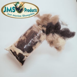 May include: A bag of brown, black, and white merino sheep wool. The wool is loose and fluffy, and it is spilling out of the bag. The bag is labeled "JMS Products Just Merino Sheepskin".