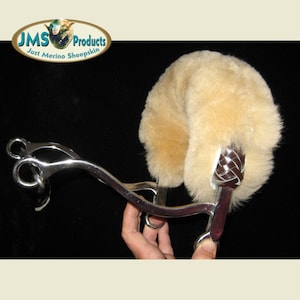 May include: A brown leather horse bit with a sheepskin cover. The sheepskin is a light tan colour and has a braided leather strap on the side. The bit is made of metal and has a silver finish.  "JMS Products Just Merino Sheepskin" is printed on a green and white logo in the top left corner of the image.