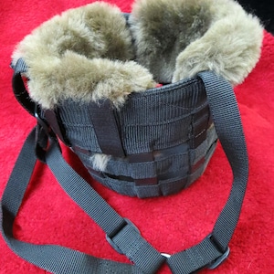 May include: Black dog muzzle with a woven design and a soft, brown fur lining around the inside. The muzzle has adjustable black straps and a metal ring for leash attachment. The product is designed for pet safety and comfort.