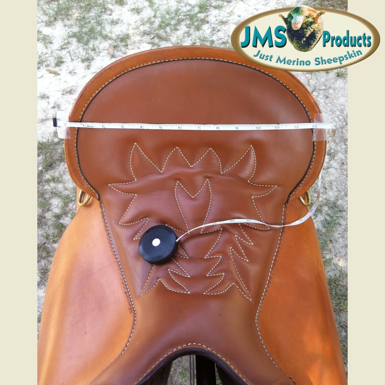 May include: A brown leather saddle with a decorative stitching pattern. The saddle is measured with a tape measure, showing a length of 17 inches. The saddle is labelled with the text "JMS Products Just Merino Sheepskin".