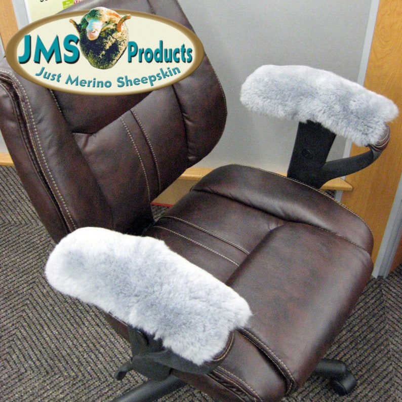 May include: Two gray sheepskin armrest covers on a brown leather office chair. The chair has a high back and adjustable arms. The chair is in a room with a carpeted floor. The armrest covers are made of soft, luxurious sheepskin and are designed to provide comfort and support. The chair is a popular choice for home offices and workspaces.