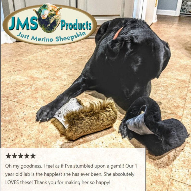 May include: A black Labrador Retriever dog laying on a light brown tiled floor with two brown sheepskin dog toys. The dog is looking to the left of the image. The text "JMS Products Just Merino Sheepskin" is visible in the top left corner of the image. The text "Oh my goodness, I feel as if I've stumbled upon a gem!!! Our 1 year old lab is the happiest she has ever been. She absolutely LOVES these! Thank you for making her so happy!" is visible at the bottom of the image.