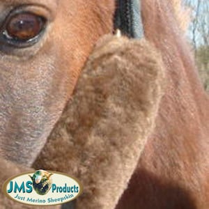 May include: Close-up of a brown horse's head with a brown sheepskin noseband. The noseband is made of soft, fluffy sheepskin and is designed to protect the horse's nose from chafing. The noseband is labeled "JMS Products Just Merino Sheepskin".