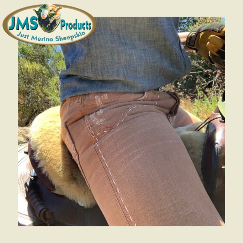 May include: A person wearing brown jeans with white stitching sits on a brown leather saddle with a sheepskin seat pad. The saddle is covered in a light brown sheepskin. The person is wearing a blue denim shirt and a brown leather glove.