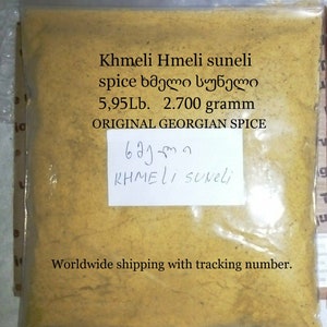 Może przedstawiać: Przezroczysta plastikowa torba wypełniona żółto-brązową mieszanką przypraw. Na torbie widnieje napis "Khmeli Hmeli suneli spice" oraz "ORIGINAL GEORGIAN SPICE". Torba zawiera 2700 gramów przypraw.
