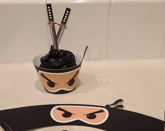May include: Black cupcake with black frosting and a ninja face cupcake wrapper. Two black swords are stuck into the frosting. A black ninja mask cupcake wrapper with a white face and two black eyes.