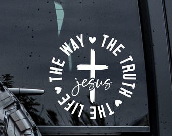 May include: White vinyl decal with a cross and the word "Jesus" in cursive. The text "The Way, The Truth, The Life" surrounds the cross, with heart symbols. Designed for application on a car window.