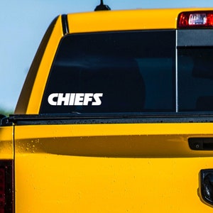 Pode incluir: Uma caminhonete amarela com um adesivo branco "CHIEFS" na janela traseira.