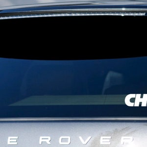 Pode incluir: Um adesivo de vinil branco com a palavra "CHIEFS" em letras brancas e negrito sobre um fundo preto. O adesivo est&aacute; na janela traseira de um carro prateado.