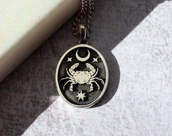 Op de afbeelding: Zilveren ketting met een ronde hanger met een gedetailleerd krabontwerp, een halve maan en sterren.