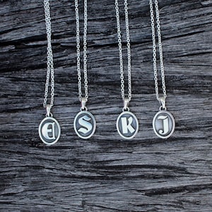 May include: Five silver necklaces with oval pendants featuring the letters E, S, K, and J in a gothic font.