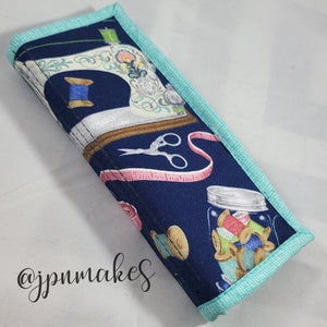 May include: A blue fabric pencil case with a sewing theme. The case features a vintage sewing machine, spools of thread, scissors, and a measuring tape. The case has a turquoise trim.