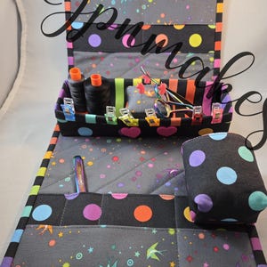 May include: A quilted fabric sewing organizer featuring a black base with colorful polka dots and swallow motifs. The set includes a rectangular tray with internal compartments, a matching pincushion, and a flat mat with pockets for tools.