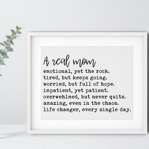 May include: A framed print with a white background and black text that reads "A real mom emotional, yet the rock. tired, but keeps going. worried, but full of hope. impatient, yet patient. overwhelmed, but never quits. amazing, even in the chaos. life changer, every single day."