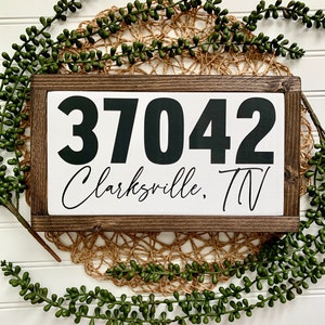 May include: A wooden sign with a white background and black lettering. The sign reads "37042 Clarksville, TN".