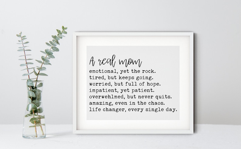 May include: A framed print with a white background and black text that reads "A real mom emotional, yet the rock. tired, but keeps going. worried, but full of hope. impatient, yet patient. overwhelmed, but never quits. amazing, even in the chaos. life changer, every single day."