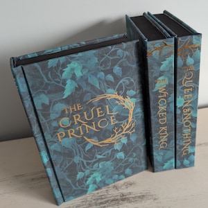 Peut inclure: Ensemble de livres de fantasy avec des couvertures assorties. Les livres ont un fond bleu-vert foncé avec un motif de feuilles et des lettres dorées. Les titres incluent "The Cruel Prince", "The Wicked King" et "The Queen of Nothing".