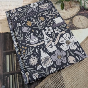 Peut inclure: Tissu bleu foncé avec un motif répété de fleurs blanches et grises, de bouteilles, de crânes et de tasses à thé. Le tissu est plié, révélant le motif. L'arrière-plan comprend une bibliothèque, une carte et de la toile de jute.