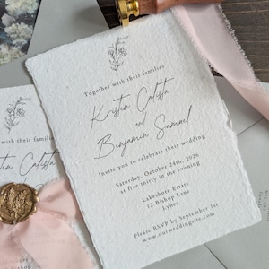 Puede incluir: Conjunto de invitaciones de boda con papel blanco texturizado, escritura negra y detalles florales. Incluye un sello de cera dorado, cinta rosa y un sello de cera con mango de madera. La invitación dice "Kristin Calista y Benjamin Samuel".
