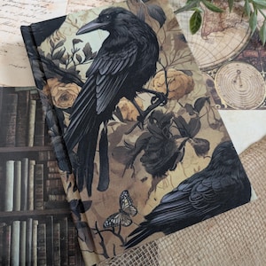 Peut inclure: Un journal décoratif avec une illustration d'un corbeau noir perché sur une branche, entouré de roses et d'un papillon. Le fond est sépia, avec une ambiance vintage et gothique.