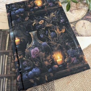 Peut inclure: Un journal sombre avec un motif floral et de bougies. La couverture présente une illustration détaillée de fleurs, de bougies et de bouteilles en verre. La palette de couleurs comprend des nuances de violet, d'or et de noir.