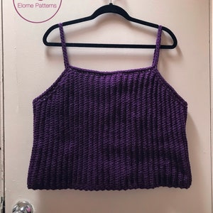 May include: A purple crochet tank top with thin straps hanging on a black hanger against a white door.