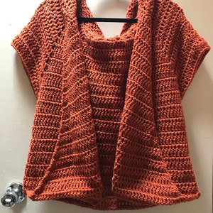 Puede incluir: Un cárdigan de ganchillo de color óxido con capucha y mangas cortas.