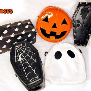 May include: A collection of Halloween-themed purses in various shapes and designs. Includes a black coffin-shaped purse with a spiderweb, a white ghost-shaped purse, and an orange pumpkin-shaped purse. The word "Purses" is written in orange text.