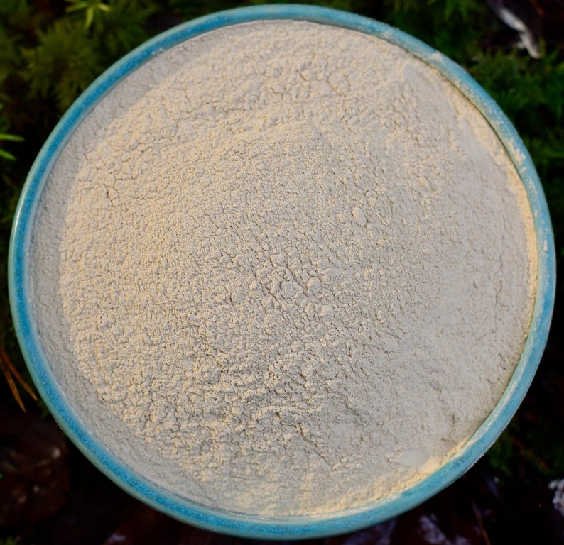 May include: A close-up view of a light beige powder in a blue ceramic bowl. The powder is smooth and fine, with a slightly grainy texture.