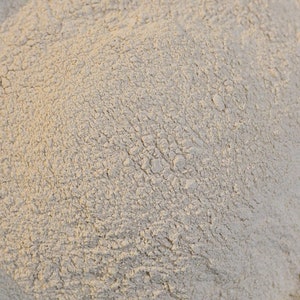 May include: A close-up view of a pile of light beige powder. The powder has a fine, granular texture and is evenly distributed throughout the image.