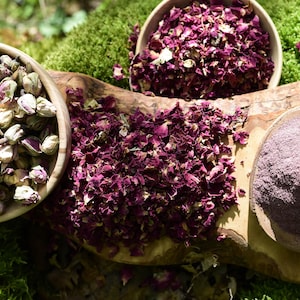 Könnte beinhalten: Draufsicht auf drei Holzschalen mit botanischen Zutaten. Eine Schale enthält getrocknete Rosenknospen, eine weitere getrocknete Rosenblätter und die dritte ein feines Rosenpulver. Die Artikel sind auf einer Holzoberfläche angeordnet.