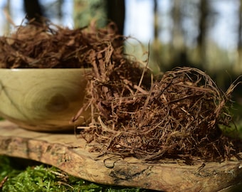 Può includere: Una ciotola di legno piena di fibre vegetali marroni secche, con altre fibre che si riversano su una superficie di legno. La ciotola e la superficie sono entrambe in legno con una venatura naturale.