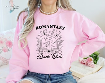 May include: Pink sweatshirt featuring a black graphic design of a book with a sword and butterflies. The text "Romantasy Book Club" is printed below the graphic.