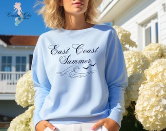 May include: A light blue sweatshirt with the text "East Coast Summer" in black cursive lettering. The design also includes a wave and two birds.