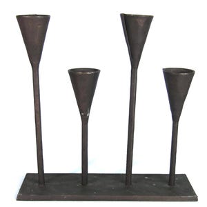 May include: A dark brown metal candle holder with four conical cups. The cups are attached to thin stems of varying heights, all mounted on a rectangular base. The candle holder is made of metal and has a rustic appearance.