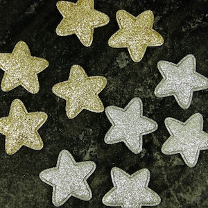 May include: Nine sparkly stars in gold and silver colours. The stars are arranged in a circle on a dark grey background.