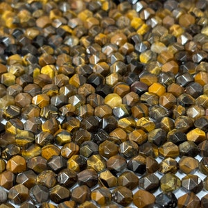 May include: A close-up of a pile of faceted tiger's eye beads. The beads are a mix of brown, gold, and black colours. The beads are all about the same size and shape.