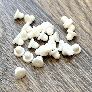 May include: A collection of small, white, mushroom-shaped objects scattered on a wooden surface. Each object has a rounded top and a flat base, resembling tiny mushrooms. The objects are made of a smooth, opaque material.