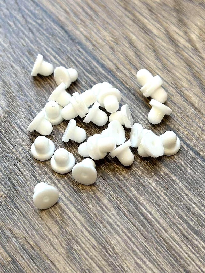 May include: A collection of small, white, mushroom-shaped objects scattered on a wooden surface. Each object has a rounded top and a flat base, resembling tiny mushrooms. The objects are made of a smooth, opaque material.
