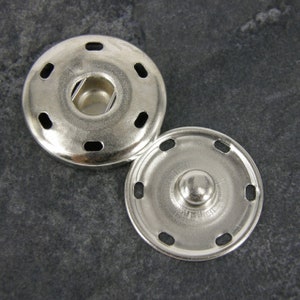 May include: Two silver metal snap fasteners, one with a raised centre and the other with a recessed centre, both with six evenly spaced holes around the edge.