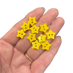 May include: A selection of bright yellow star-shaped buttons. Each button has two holes for sewing. The buttons are a cheerful yellow colour and are ideal for craft projects, sewing, or adding a decorative touch to clothing.