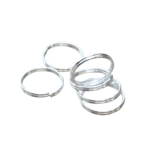 May include: A selection of silver split key rings. The key rings are made of metal and are circular. Some rings are open, while others are closed and stacked together. The background is white.