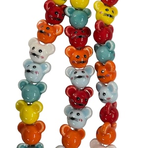 May include: Close-up of three strands of colourful ceramic beads shaped like mice. The beads are in various colours, including red, orange, yellow, blue, and white. Each mouse bead has black eyes and whiskers.